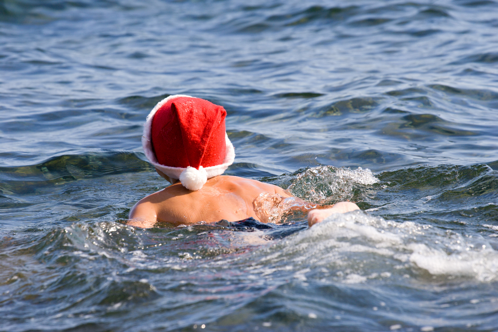 Jongen zwemt in het water met een kerstmuts op