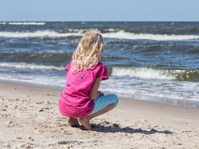 Kind gehurkt in het zand kijkt uit over de zee