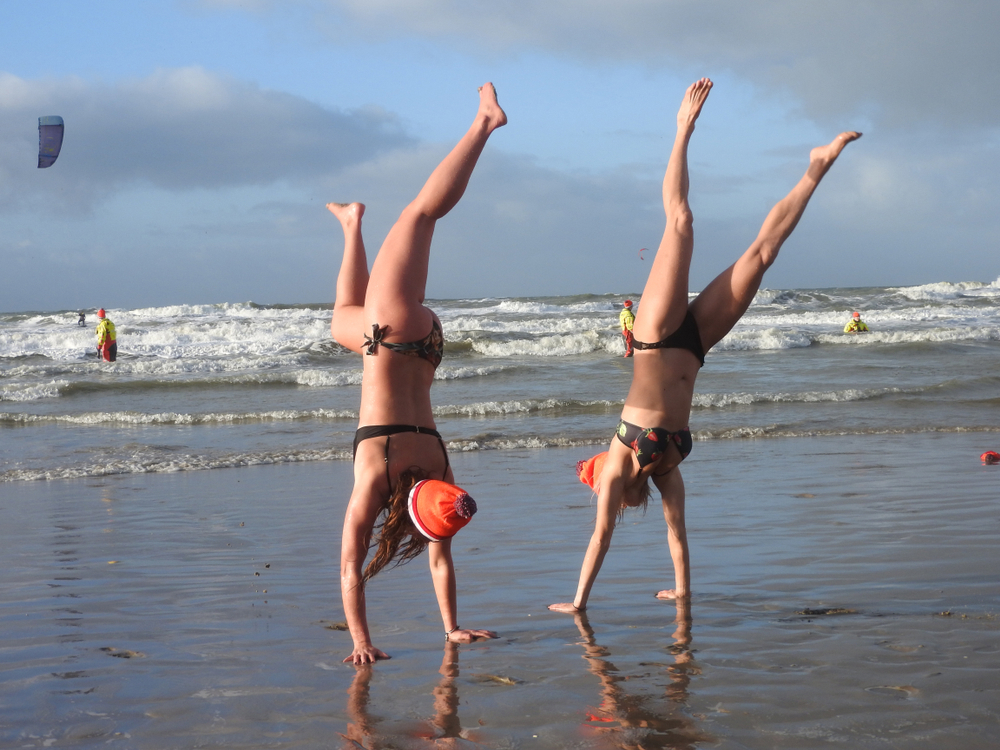 Twee meiden met een muts en bikini doen de handstand op het strand tijdens de nieuwsjaarsduik
